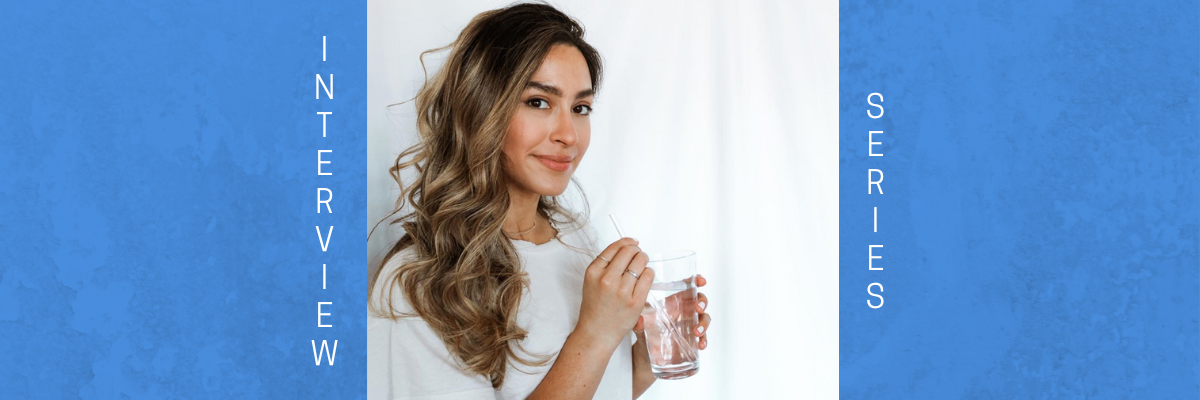 Lauren Nowicki smiling at the camera wearing a white shirt on a white background. She is holding a clear glass of water with a straw in it.