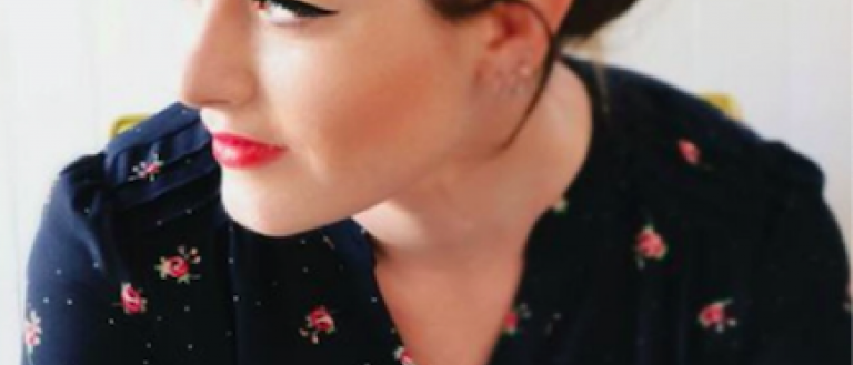 Image Description: A photo of Mandy Harvey. She looks away from the camera, over her right shoulder. She wears a black top with a pattern of small roses on it. 