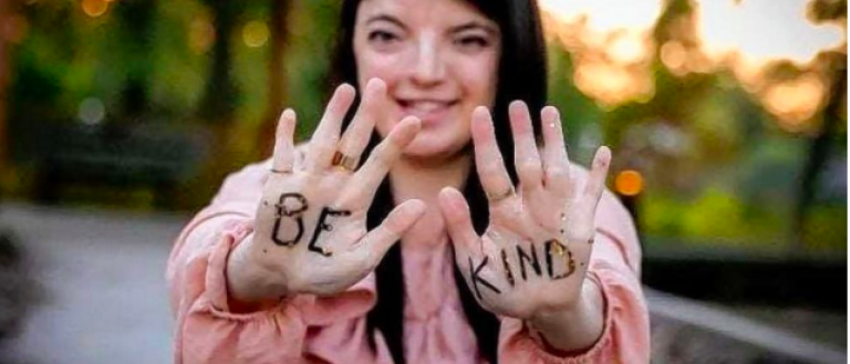 Image Description: Rena Rosa holds up her hands to the camera. Written on them are the words: "Be Kind." 