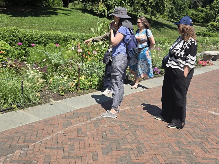 Three people stand on a brick pathway next to a garden and lawn