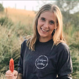 An image of Kathryn Jenkins. She smiles for the camera, holding a popsicle, standing in a meadow. 