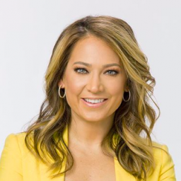 Image Description: A photo of Ginger Zee. Ginger smiles at the camera, with her arms folded across her chest. She wears a yellow suit jacket. 