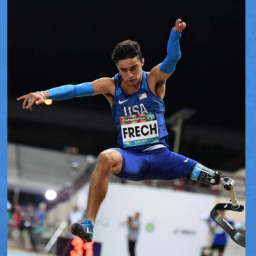 Image of Ezra Frech. He is 15 years old and has congenital limb deficiencies. Ezra is jumping high in his USA Paralympic uniform.  Ezra is scheduled to compete in long jump, high jump, and the 100 [meters]. He has brown hair and a determined look on his face.