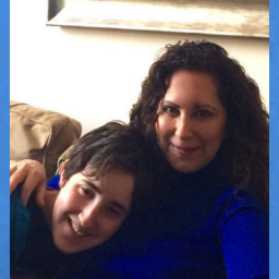 Image of Judith Newman and her son Gus, who is autistic. They are sitting on a brown couch in an embrace, while smiling at the camera.