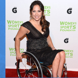 Image of Paralympic basketball player Alana Nichols attends the 33rd Annual Salute to Women in Sports Gala at Cipriani Wall Street on October 17, 2012 in New York City. Alana is on the red carpet in her wheelchair. She is dressed in a short black dress, which has a sparkle appearance. Her brown hair is pulled into a side low ponytail.