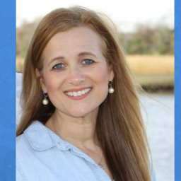 Image of Edie Cusack. She is looking at the camera and is positioned on the left side of the photo. the background is a water scene, but it is muted. Edie has long dirty blonde hair, fair skin, and is wearing a white button-up shirt..