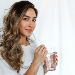 Lauren Nowicki smiling at the camera wearing a white shirt on a white background. She is holding a clear glass of water with a straw in it.