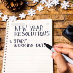 A pair of hands, one holding a pen over a pad, that reads "New Year Resolutions, start working out"