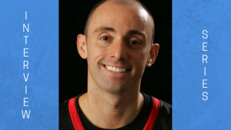Image of MIke Simmel. The image is of a bald man, with a big smile. He is wearing a black shirt with red trim.