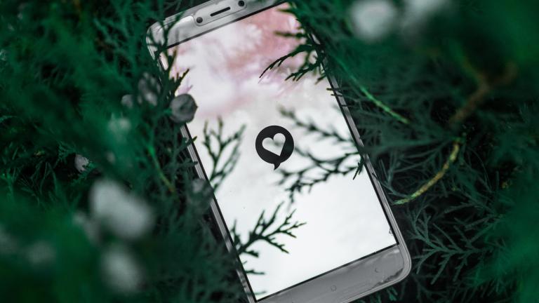 Cell phone in the grass. Lighted screen displaying white background with white heart.